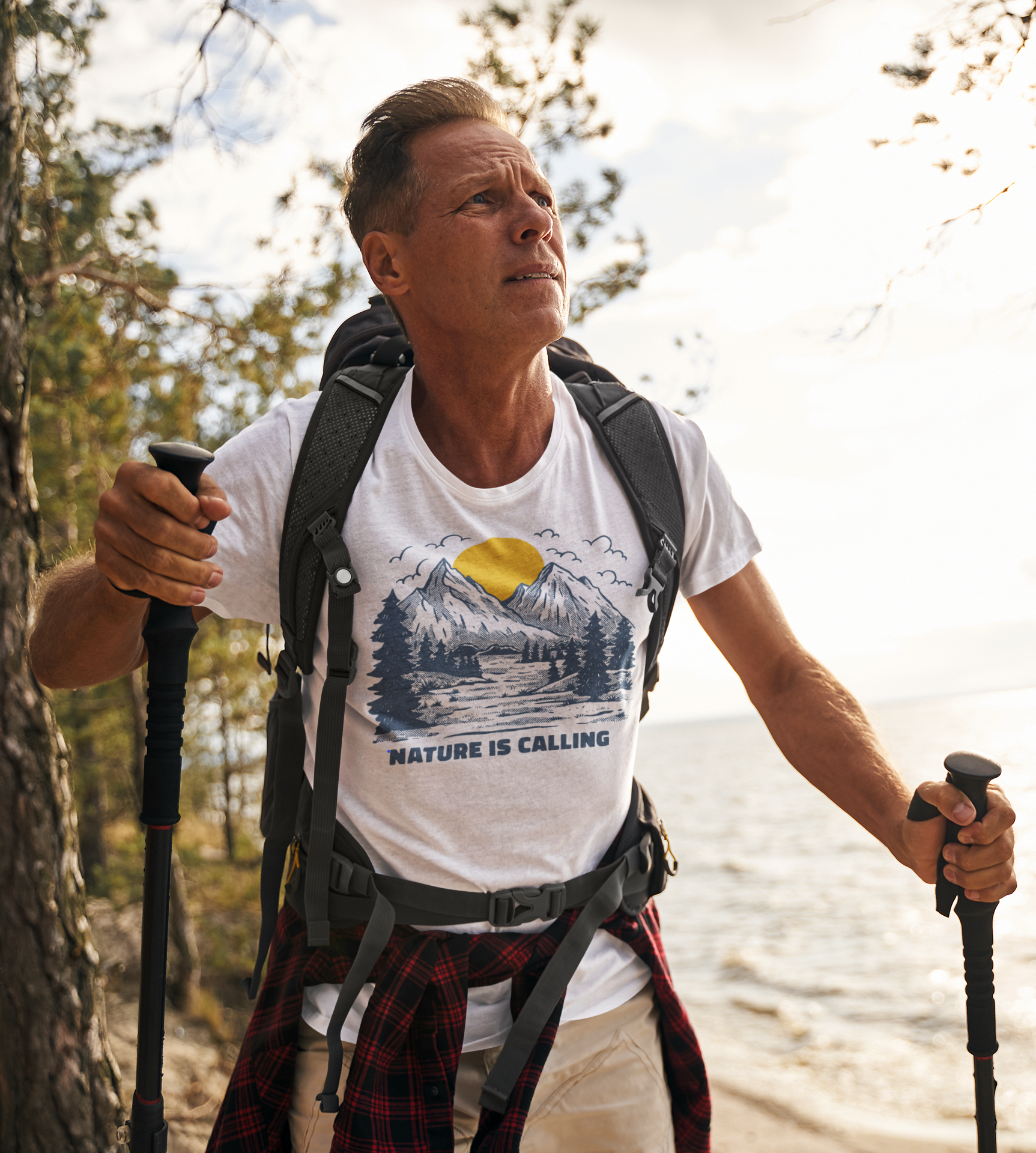 Man outdoors hiking wearing a t-shirt from My Weekend Tees that has an image of mountains and sunset with quote Nature is Calling